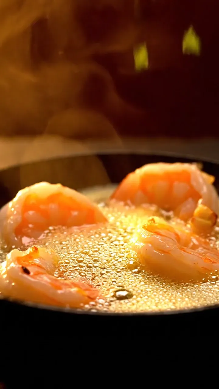 Prawns sizzling in garlic butter as herbs fall in slow motion