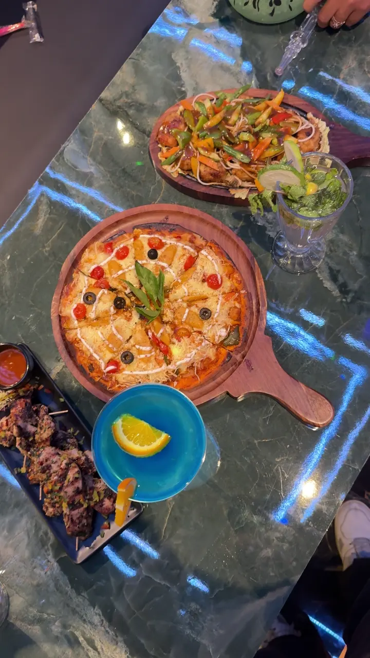 A loaded pizza, a sizzler and a mint mocktail on the green marble table